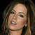 A pixelated close-up of a person with light skin tone, brown hair, and pink lips, mouth open in mid-speech against a dark background.