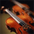 Pixelated image of a violin with a bow, rendered in warm orange and brown tones against a dark background.