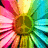 A vibrant, pixelated flower with radiating petals in pink, yellow, green, and cyan hues arranged around a brown center.