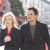 Two people stand side-by-side in a pixelated image; the person on the left has blonde hair and wears a dark jacket over a red top, while the person on the right has dark hair and wears a dark jacket over a gray top.