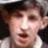 Pixelated close-up of a person's face with light skin tone, dark hair, and mouth open in mid-expression against a dark background.