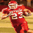 Pixelated image of a football player in red uniform with white helmet and number 25, holding a ball on a field.