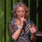 25 identical frames showing a woman with blonde hair in a black-and-white polka-dot dress holding a microphone against green vertical stripes