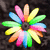 A static pixelated flower with multicolored petals radiating from a dark center against a black background.