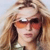 Pixelated close-up of a person with long light brown hair wearing dark sunglasses and a green top against a light background.