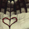 A hand forms a heart shape with red beaded bracelets on a white fabric background.