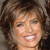 A pixelated close-up of a person with curly brown hair, light skin, and a wide open mouth showing teeth, set against a blurred background.