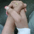 A pair of hands clasped together with fingers interlocked, showing a ring on one finger and white wristbands.
