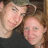 Two people in close proximity, one with light skin and dark hair leaning toward another person with lighter skin and brown hair against a blurred background.