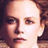 Pixelated close-up of a person's face with visible eyes, nose, mouth, and hair in warm tones on a dark background.