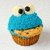 Pixelated blue and brown cupcake with two large black eyes on top, set against a light gray background.