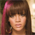 A static pixelated image of a person with long brown hair featuring a pink streak on the left side, wearing a dark top against a blurred background.