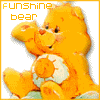 A static orange Care Bear with a white sun emblem on its belly, holding one paw up near its face against a white background.