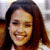 Pixelated close-up of a person with long dark hair, closed eyes, and a smiling mouth against a blurred background.