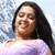Static pixelated image of a person with long dark hair wearing a light purple top against a blurred background.