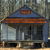 Static pixel art of a blue building with a brown roof and a small red sign, set against a blurred background.
