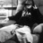Pixelated grayscale image of a figure in dark clothing holding an object, with partial text visible on the chest area.