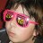 A pixelated close-up of a person wearing pink sunglasses with green-tinted lenses, set against a dark blurred background.