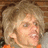 Pixelated close-up of a person with light brown curly hair, wearing an orange garment against a blurred background.