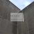Pixelated static image showing a light gray rectangular sign mounted on a dark pole between two sloped, textured walls under a pale blue sky.