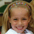 Pixelated close-up of a smiling person with light brown hair tied in pigtails, wearing a white top against a blurred background.