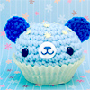 A pixelated cupcake-shaped icon with blue frosting, yellow star sprinkles, and dark blue ears, set against a light blue background with pink and white snowflakes.