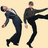 Two pixelated figures in dark suits against a beige background, one leaning forward with arms extended, the other standing with one leg kicked out and arm extended.