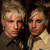 Two identical blonde individuals in military-style uniforms appear side-by-side with a green text overlay reading 'Madina Lake' on the right.