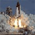 A rocket launches with bright flames and smoke against a blue sky background, captured in a pixelated static image.