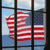 A pixelated American flag viewed through a grid of dark-framed panes, with blue sky and water visible behind the flag.