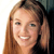 A pixelated close-up of a person with long light brown hair, smiling with visible teeth, against a light background with dark areas on the right.