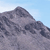 Pixelated mountain peak with layered gray and dark blue tones against a light blue sky background.