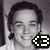 Pixelated grayscale portrait of a person with dark hair, closed eyes, and a slight smile, featuring a black-and-white checkered symbol in the bottom-right corner.