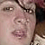 Pixelated close-up of a person's face with visible eyes, nose, mouth, and dark hair against a light background.