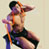 Pixelated static icon of a shirtless man with dark hair and beard sitting on a chair, wearing black shorts and an orange strap across his chest, against a light beige background.