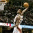 Pixelated image of a basketball player in mid-air shooting a ball, wearing white uniform with red accents and dark shorts.