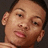 Pixelated close-up of a person's face with light skin tone, dark hair, and visible ear against dark background.