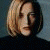 A static image of a person with short blonde hair wearing a dark turtleneck against a blue background.