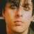 Pixelated close-up of a person's face with light skin tone, brown eyes, and short dark hair against a dark background.