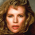 Pixelated close-up of a person with light brown curly hair, neutral expression, and visible facial features including eyes, nose, and lips.