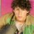 Pixelated image of a person with dark brown hair, light skin, and closed eyes against a pink background wearing layered clothing.