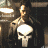 A character in a dark jacket holds a white skull symbol against a dimly lit background with visible ceiling lights.