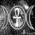 Monochrome icon featuring a central ankh symbol surrounded by stylized hieroglyphic-like shapes on a pixelated background.