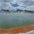 Pixelated landscape with blue sky, scattered clouds, dark horizontal bands, greenish water, and brown shoreline.