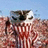A pixelated image shows a figure with dark hair and light skin holding a large, striped object against a blue sky background.