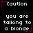 Pixelated text displays 'Caution you are talking to a blonde' with red star accents on a black background.