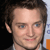 Pixelated close-up of a person with brown hair, light skin, and blue eyes, wearing a light-colored shirt against a dark background with partial blue and orange elements.
