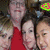 Three people in a group photo with one person wearing red clothing, set against a dark background.