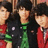 Three pixelated figures in dark clothing with green accents stand side-by-side against a blurred background.