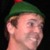 Pixelated close-up of a person wearing a green cap with a red tip, set against a dark background.